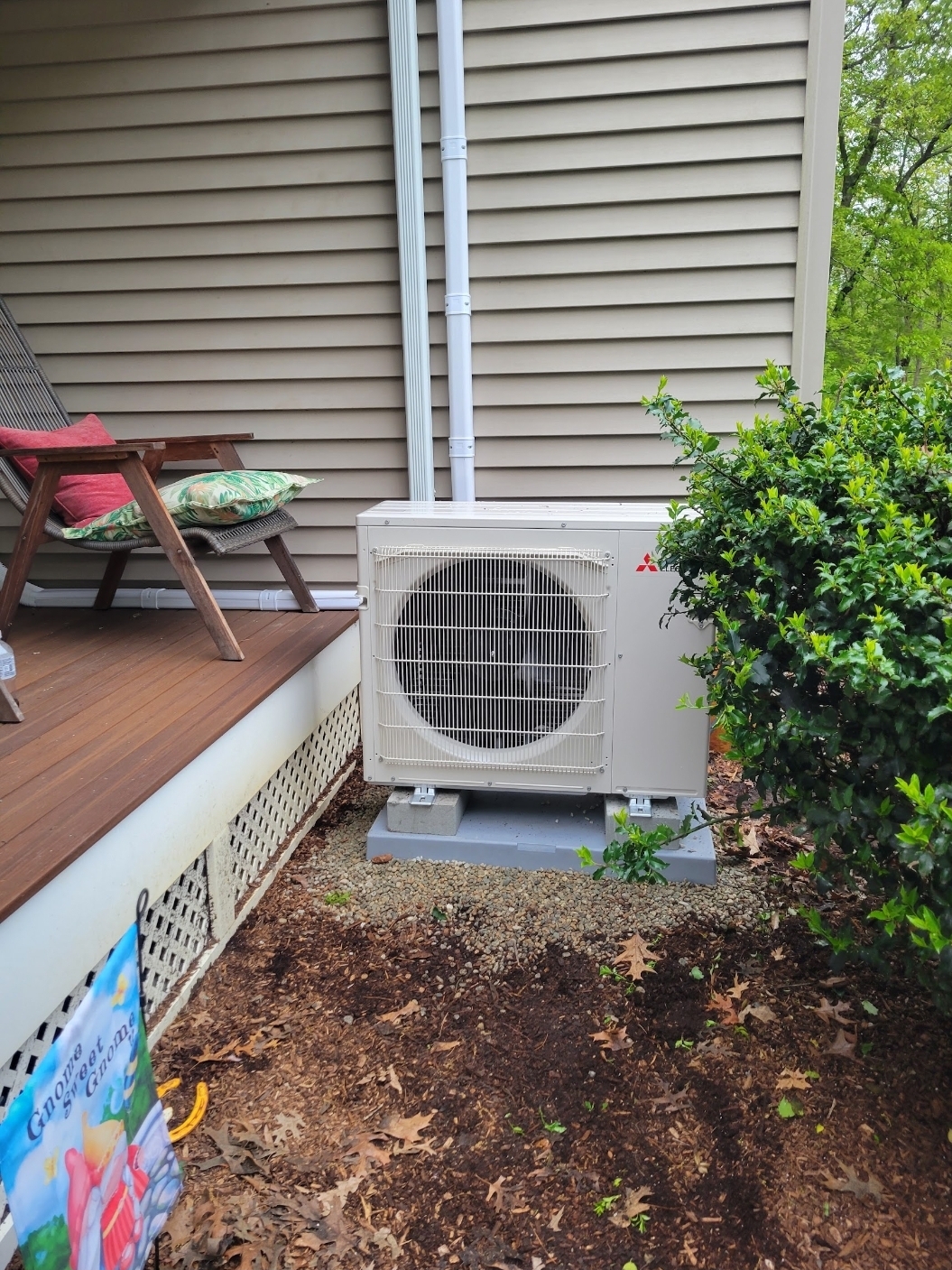 Mitsubishi heat pump outdoor unit on a gravel pad beside a home's deck