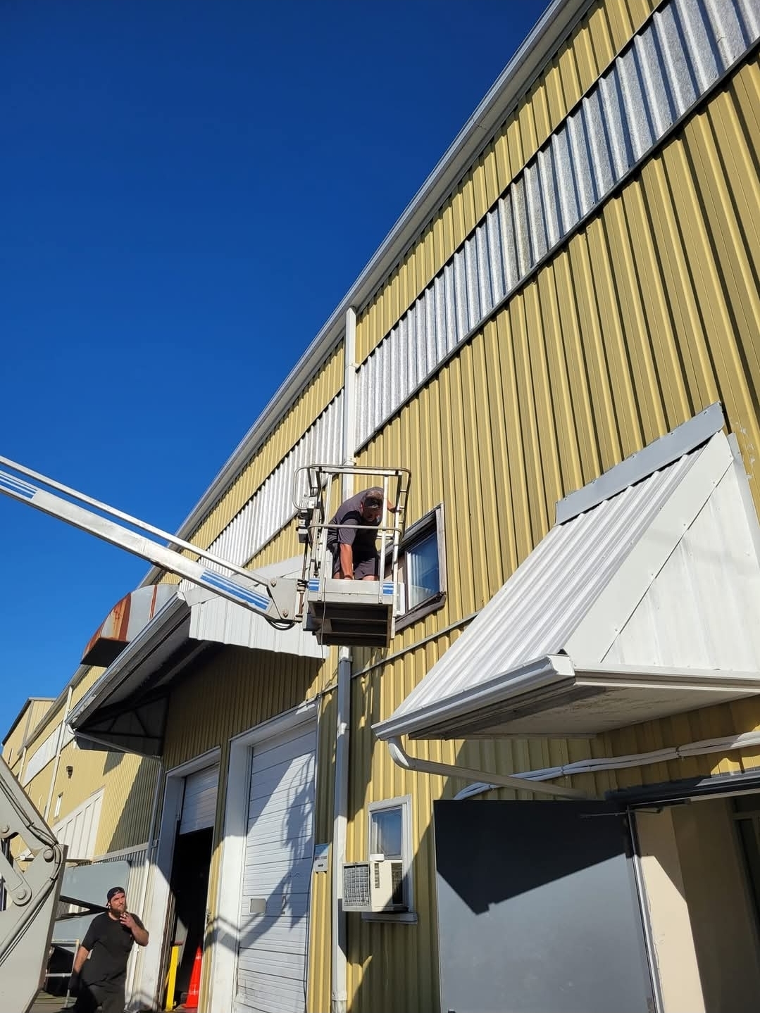 Technician in a boom lift working at the upper wall of a commercial building